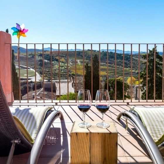 Terrassa de l’Hotel Cal Llop amb dues copes de vi i vistes a les vinyes del Priorat. L’Art de Vivre.